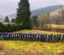 Viele Radfahrer stehen in einer Reihe auf einer Wiese, im Hintergrund Upl&auml;nder Berge