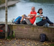 Radfahrer sitzen auf einer Mauer, die Diemel im Hintergrund