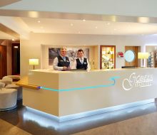 Hinter dem Rezeptionstresen stehen zwei freundliche M&auml;nner 